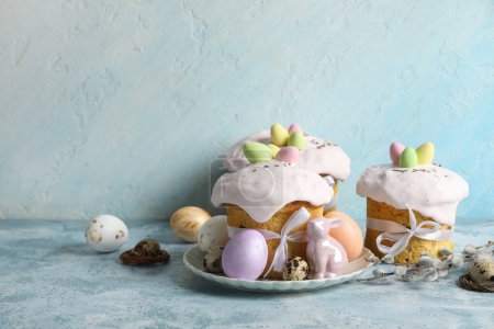 Composition with delicious decorated Easter cakes, porcelain bunny and painted eggs in plate on color background