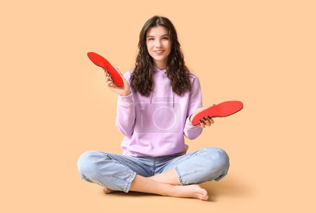 Photo for Young woman holding orthopedic insoles on beige background - Royalty Free Image