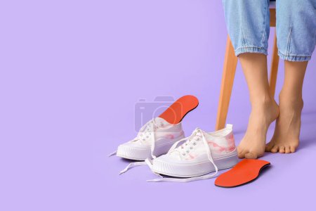 Photo for Female legs near orthopedic insoles and sneakers on lilac background, closeup - Royalty Free Image