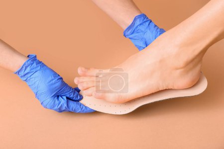 Photo for Doctor hands in medical gloves fitting orthopedic insoles to female legs on beige background, closeup - Royalty Free Image