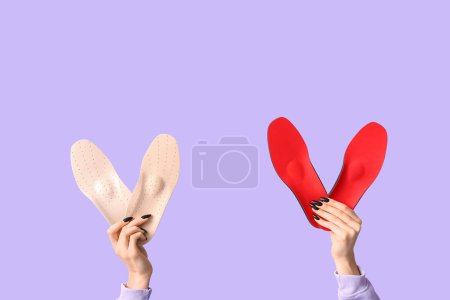 Photo for Female hands holding two pairs of orthopedic insoles on lilac background - Royalty Free Image