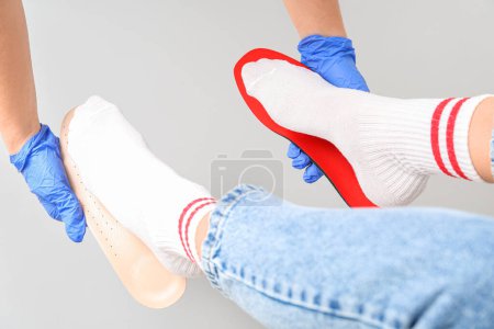Photo for Doctor hands in medical gloves fitting orthopedic insoles to female feet isolated on white background - Royalty Free Image