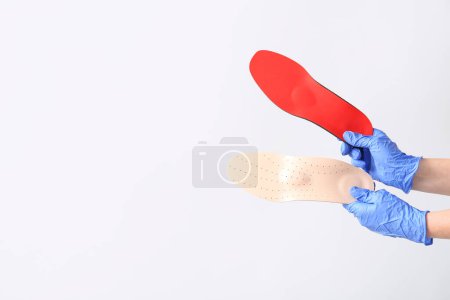 Téléchargez les photos : Les mains du médecin dans des gants médicaux tenant des semelles orthopédiques isolées sur fond blanc - en image libre de droit