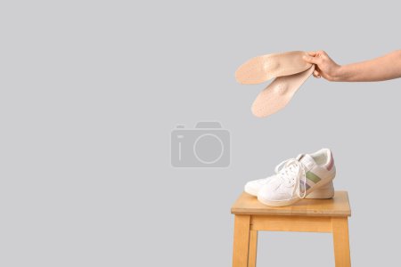 Téléchargez les photos : Chaise avec baskets et mains féminines tenant des semelles intérieures orthopédiques isolées sur fond blanc - en image libre de droit
