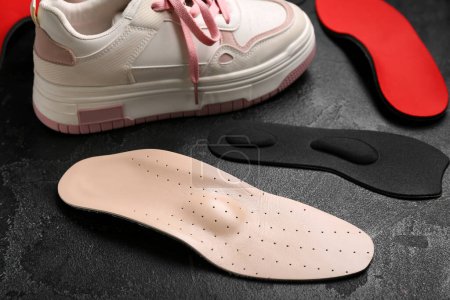 Photo for Sneakers and different orthopedic insoles on black grunge background - Royalty Free Image