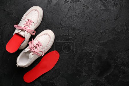 Photo for Sneakers and red orthopedic insoles on black grunge background - Royalty Free Image
