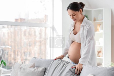 Photo for Young pregnant woman fluffing cushion at home - Royalty Free Image