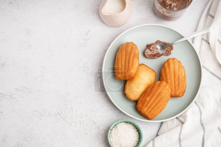 Plate with delicious madeleines and spoon with chocolate cream on light background