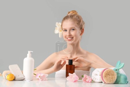 Photo for Beautiful young woman with spa supplies, Easter decor and tulip flowers at table against grey background - Royalty Free Image