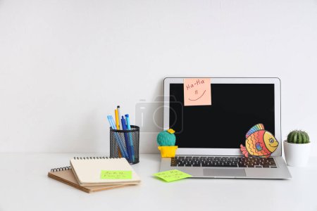 Arbeitsbereich mit Laptop, lustigen Notizen und Papierfischen auf weißem Hintergrund. Aprilscherz