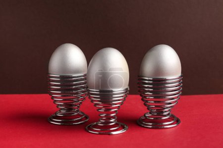 Painted eggs in egg holders on red table against brown background