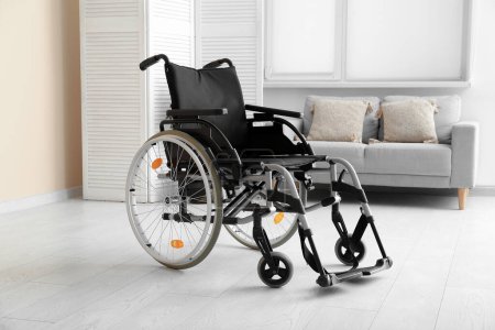 Foto de Moderna silla de ruedas vacía con pantalla plegable y sofá en el salón - Imagen libre de derechos