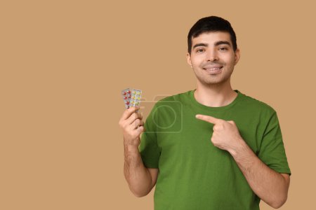Foto de Hombre joven señalando ampollas de píldoras de vitamina A sobre fondo beige - Imagen libre de derechos