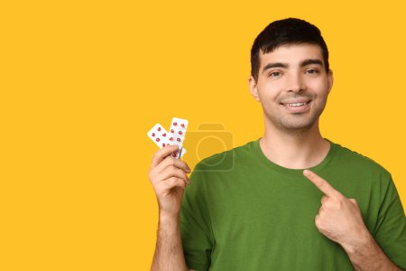 Foto de Hombre joven señalando ampollas de píldoras de vitamina A sobre fondo amarillo - Imagen libre de derechos