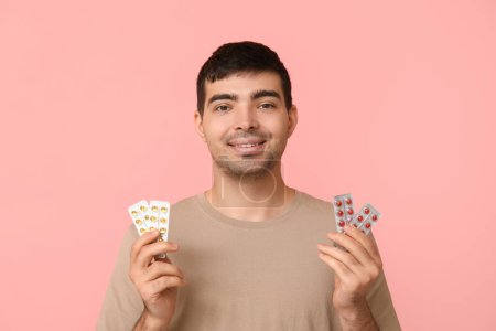 Young man with blisters of vitamin A pills on pink background