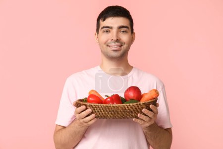 Junger Mann mit einem Korb voller Vitamin A auf rosa Hintergrund