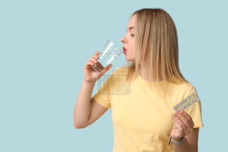 Mujer joven con pastillas de vitamina A y vaso de agua sobre fondo azul