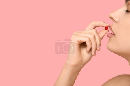 Jolie jeune femme prenant de la vitamine A capsule sur fond rose, gros plan