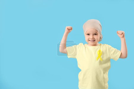 Téléchargez les photos : Petite fille après chimiothérapie avec ruban montrant les muscles sur fond bleu. Concept de sensibilisation au cancer chez l'enfant - en image libre de droit