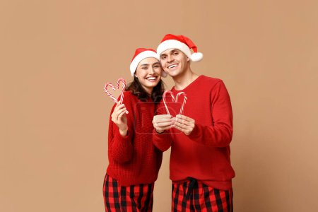 Foto de Feliz pareja joven en pijama de Navidad y con bastones de caramelo sobre fondo beige - Imagen libre de derechos