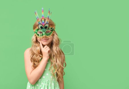 Photo for Thoughtful little girl wearing carnival mask on green background - Royalty Free Image