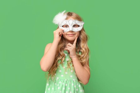 Photo for Thoughtful little girl wearing carnival mask on green background - Royalty Free Image