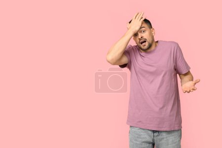Handsome worried young man covering face with hand on pink background