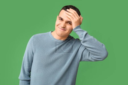 Photo for Handsome ashamed young man covering face with hand on green background - Royalty Free Image