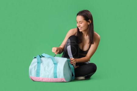 Téléchargez les photos : Jeune femme sportive avec sac assis sur fond vert - en image libre de droit