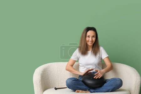 Schöne reife Frau mit Glukophon sitzt auf dem Sofa vor grünem Hintergrund