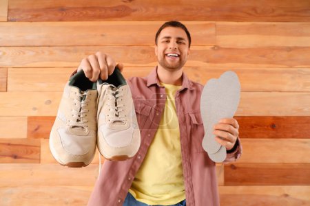 Male shoemaker with sneakers and insoles on wooden background