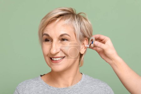 Mujer joven poniendo audífono en el oído de la mujer madura sobre fondo verde