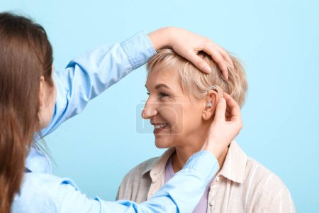 Mujer joven poniendo audífono en el oído de la mujer madura sobre fondo azul