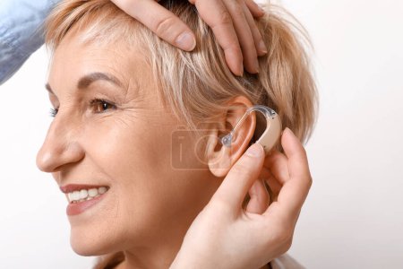 Mujer joven poniendo audífono en la oreja de la mujer madura sobre fondo blanco, primer plano
