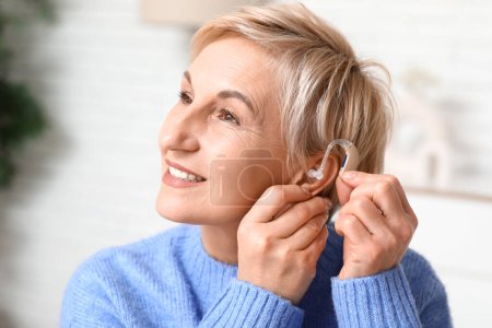 Reife Frau setzt Hörgerät auf ihr Ohr im Zimmer