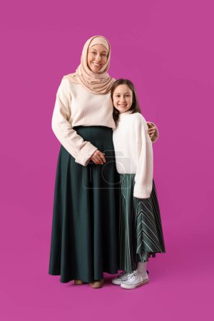 Happy Muslim mother and her daughter on pink background. Eid al-Fitr celebration
