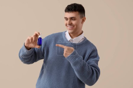 Young man pointing at bottle of CBD oil on light background