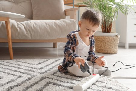 Little boy with plug and extension cord at home. Child in danger