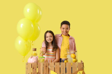 Cute little children hugging at lemonade stand on yellow background