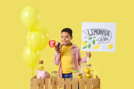 Little African-American boy with megaphone and price at lemonade stand on yellow background
