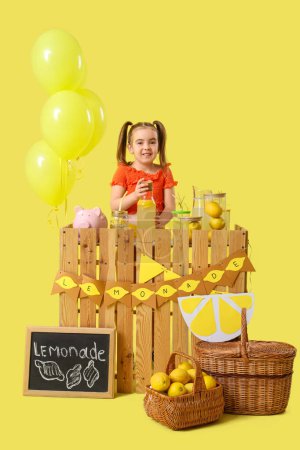 Cute little girl at lemonade stand on yellow background