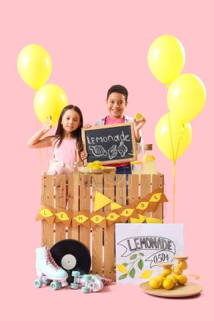 Cute little children with chalkboard and lemons at lemonade stand on pink background