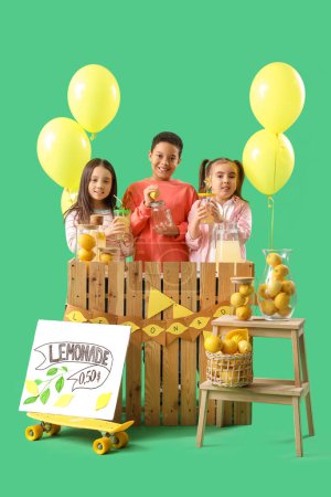 Cute little children at lemonade stand on green background