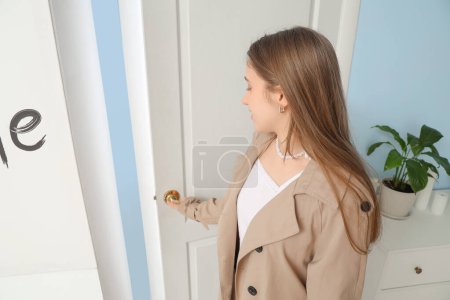 Foto de Mujer joven en gabardina cerrando la puerta en casa - Imagen libre de derechos