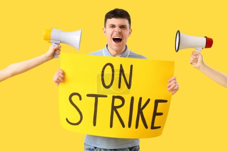 Photo for Protesting young man holding placard with text ON STRIKE and megaphones against yellow background - Royalty Free Image