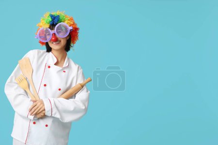 Foto de Divertido joven chef con utensilios de cocina sobre fondo azul. Día del Loco - Imagen libre de derechos