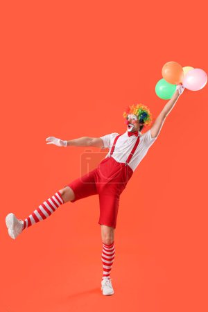Porträt eines überraschten Clowns mit Luftballons auf orangefarbenem Hintergrund. Aprilscherz-Feier