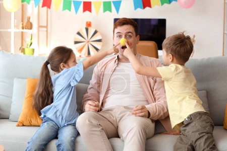 Photo for Little children pranking their father with clown nose and face paintings at home. April Fool's Day prank - Royalty Free Image
