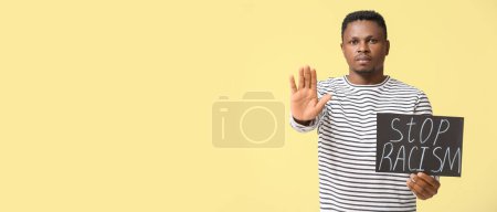 Téléchargez les photos : Homme afro-américain avec affiche montrant geste d'arrêt sur fond jaune avec espace pour le texte. Arrêtez le racisme - en image libre de droit