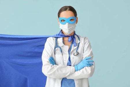 Belle femme médecin en costume de super-héros et masque médical sur fond bleu